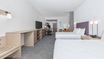 Una habitación de hotel moderna con dos camas, un escritorio, un televisor y una pequeña zona de trabajo.