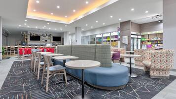 A modern cafe with round tables, red chairs, and a blue seating area.