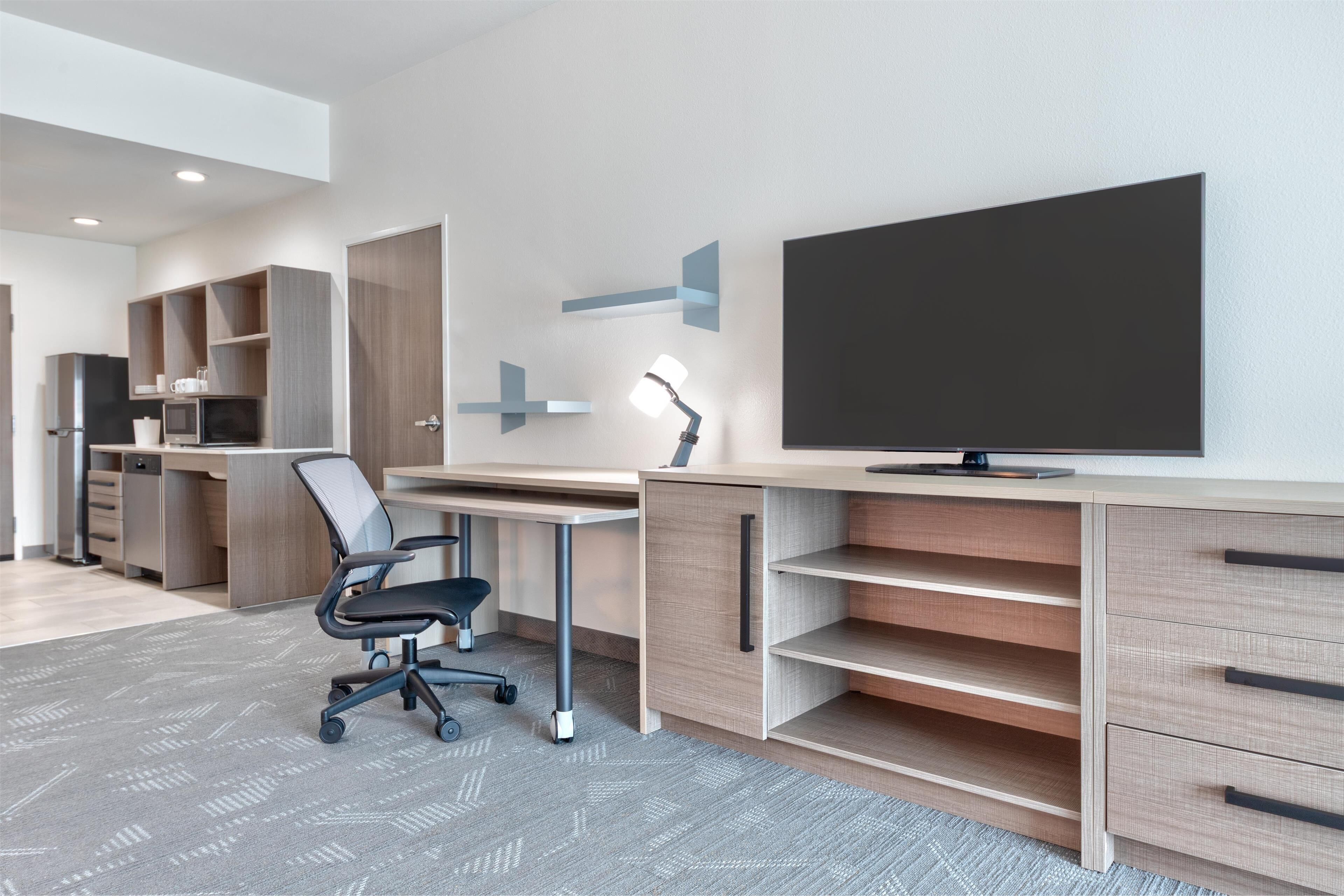 A modern office space with a large desk, ergonomic chair, built-in shelving, and a flat-screen TV.