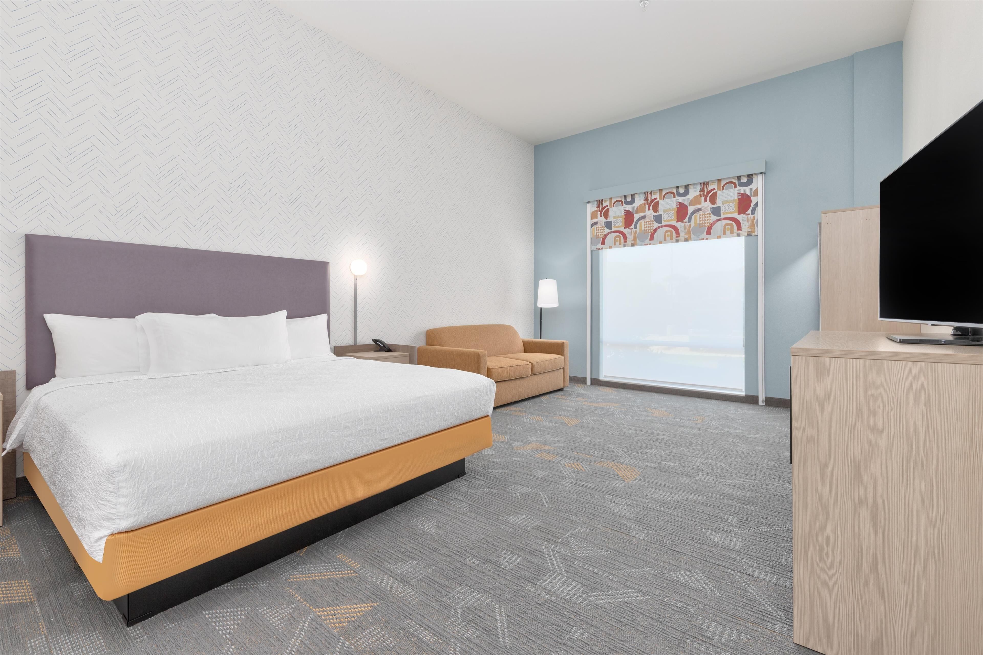 A hotel room with a bed, a desk, a chair, and a television.