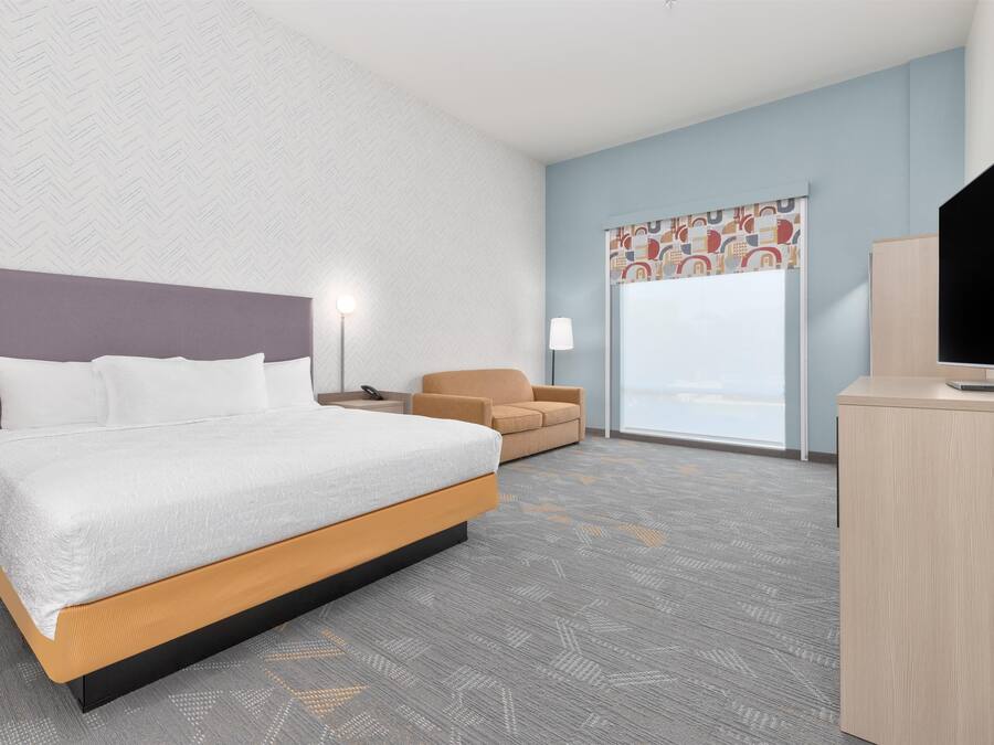 A hotel room with a bed, a desk, a chair, and a television.