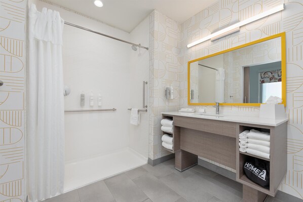 Une salle de bain moderne équipée d’une douche, d’un meuble-lavabo avec miroir et d’un porte-serviettes.