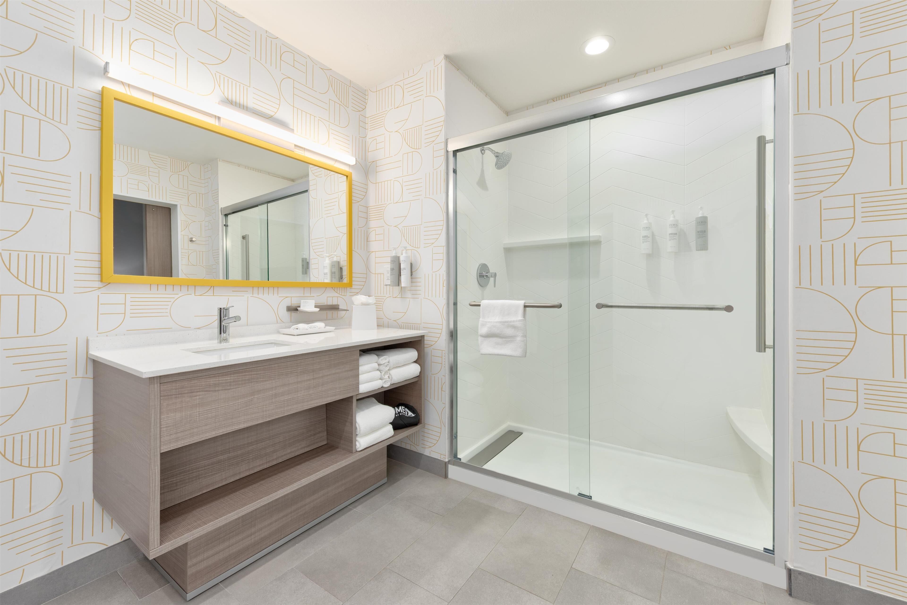 A modern bathroom with a glass shower enclosure, a white sink with a mirror, and a wooden vanity.