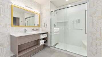 A modern bathroom with a glass shower enclosure, a white sink with a mirror, and a wooden vanity.