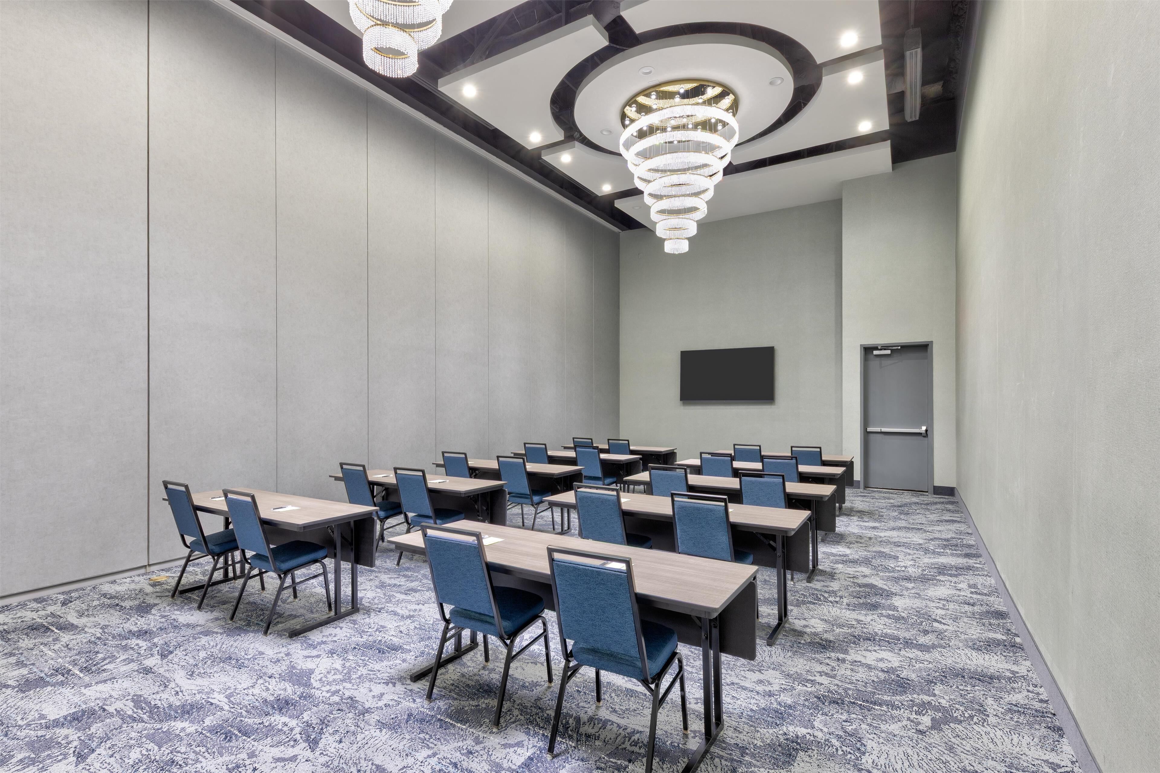 A conference room with multiple tables and chairs, a large screen, and a chandelier.