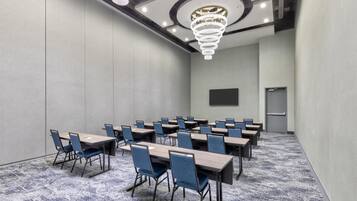 A conference room with multiple tables and chairs, a large screen, and a chandelier.
