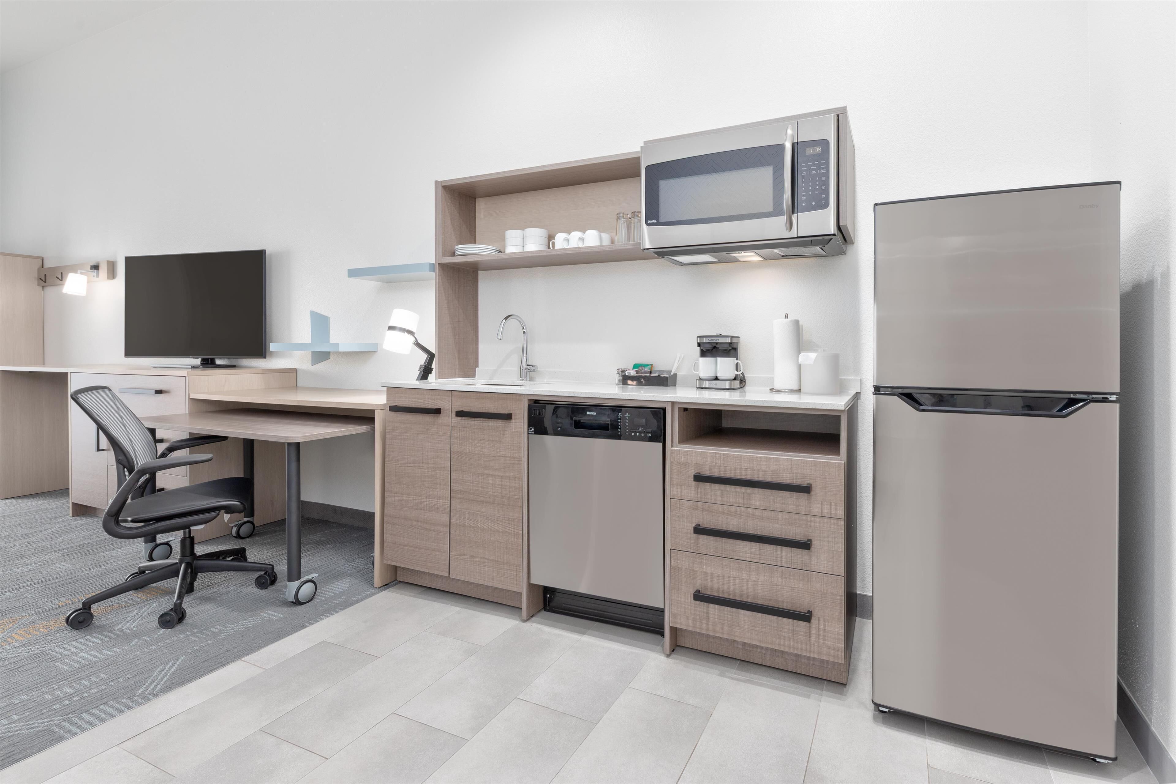 A modern kitchen with a dishwasher, microwave, refrigerator, and a flat-screen TV.