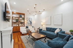 A living room with a blue sofa, white armchairs, a wooden coffee table, and a chandelier.