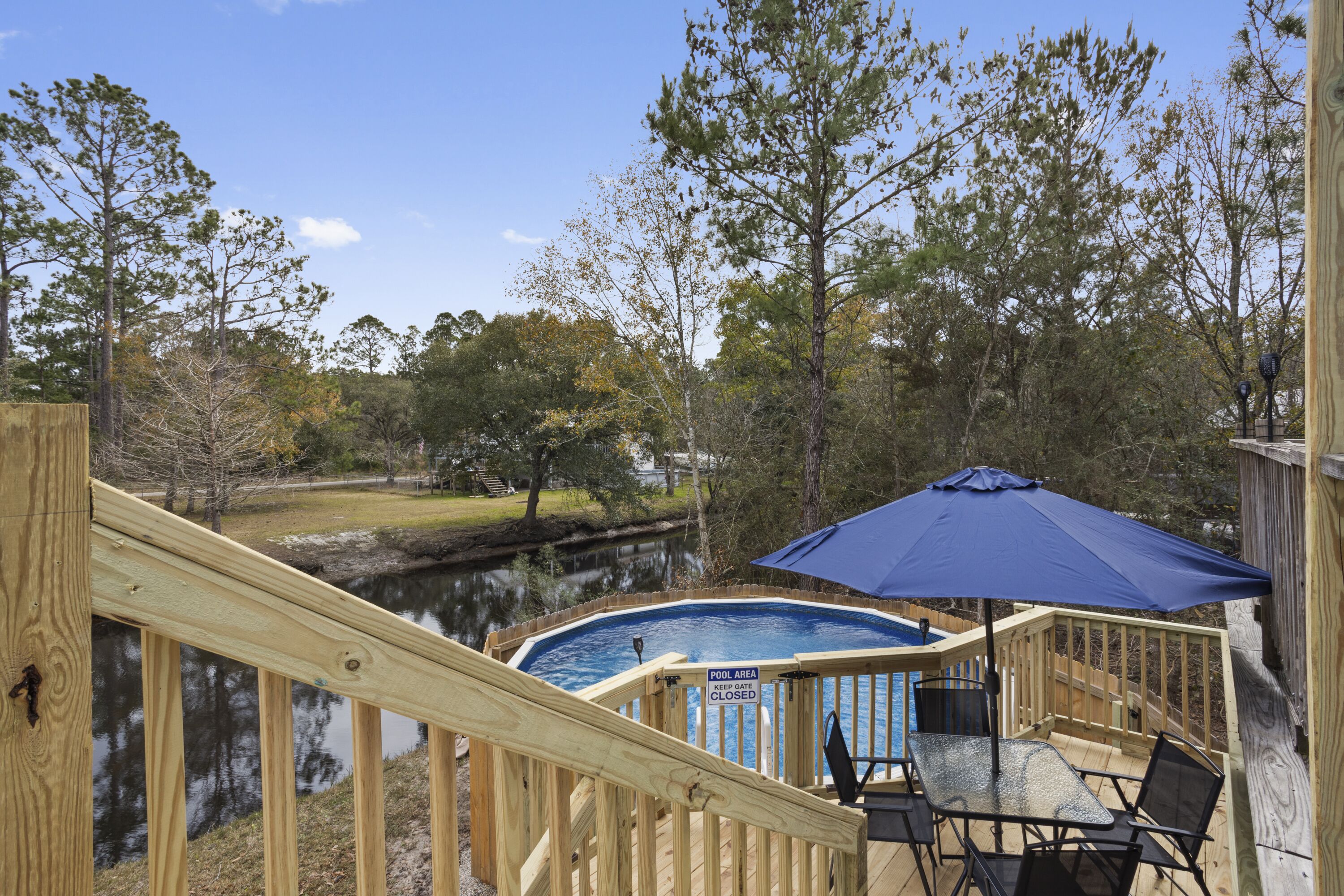 A wooden deck with a pool, a blue umbrella, and a view of a lake.