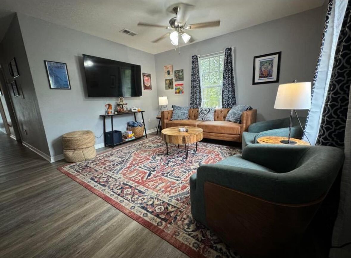 Ein Wohnzimmer mit Sofa, Sesseln, Couchtisch und einem flachbildfernseher an der Wand.