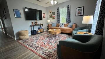 Ein Wohnzimmer mit Sofa, Sesseln, Couchtisch und einem flachbildfernseher an der Wand.