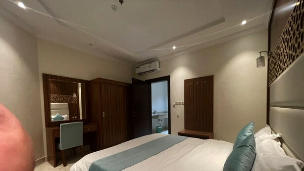 A modern bedroom with a large bed, a desk, and a wardrobe.