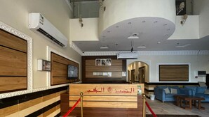 A hotel reception area with a wooden reception desk, red velvet ropes, marble flooring, and a blue sofa in the background.