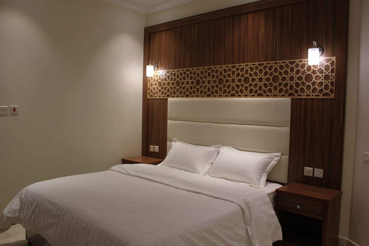 A hotel room with a large bed, wooden headboard, two bedside tables, and wall-mounted lights.