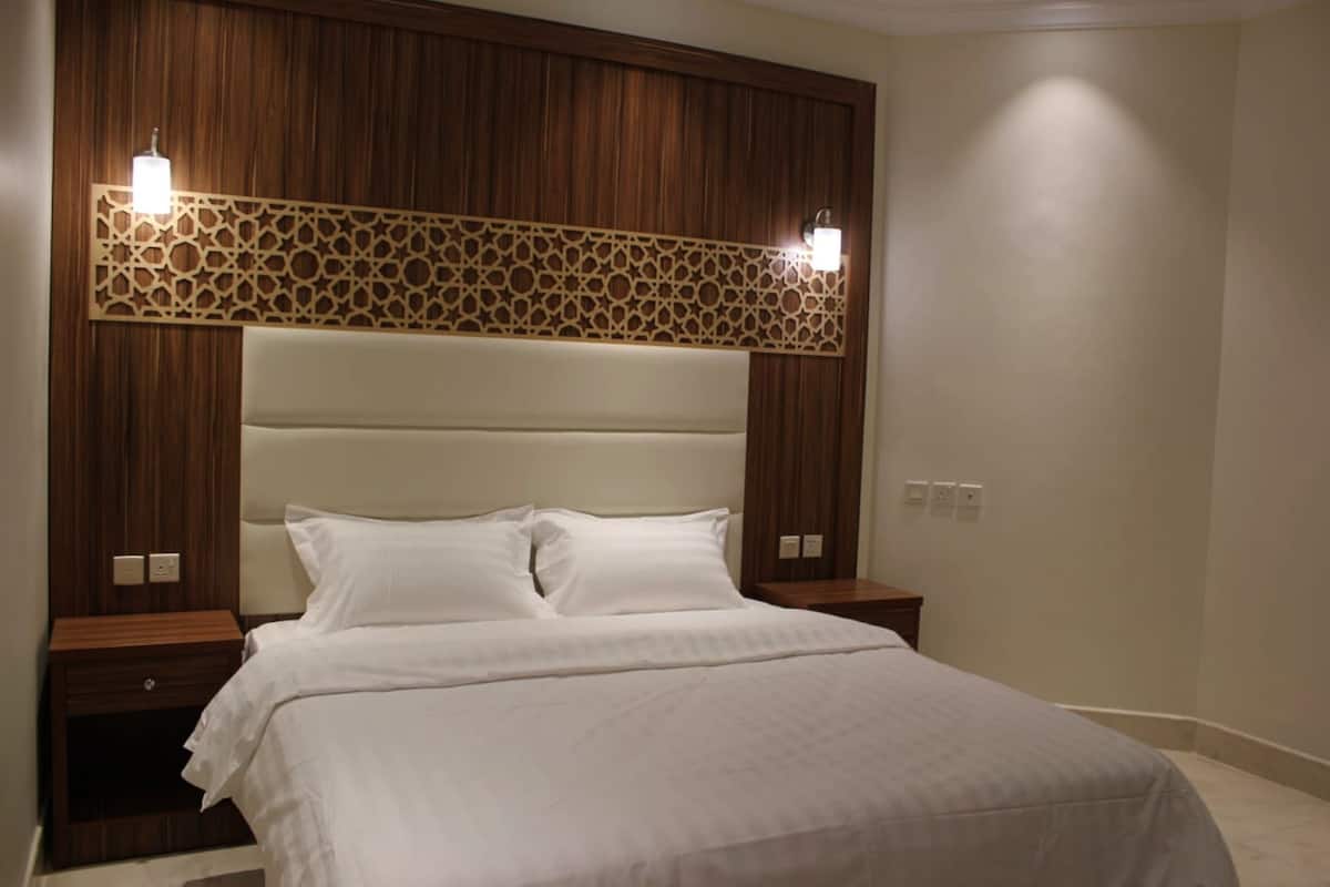 A bedroom with a large bed, wooden headboard, two bedside tables, and wall-mounted lights.