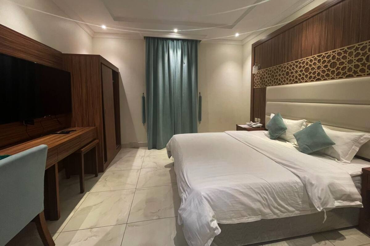 A hotel room with a bed, a TV, a desk, and a curtain.