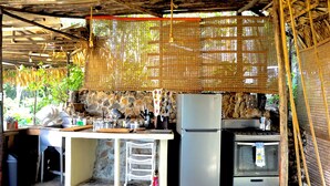 Una cocina rústica al aire libre con pared de piedra, refrigerador, estufa y plantas colgantes.
