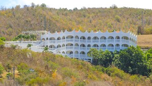 A white building with multiple balconies and arched windows, surrounded by trees and hills. - Island Castle Rentals - Saltwater Pool & Hot Tub- Lovely 3 Bedrooms  (Frederiksted)