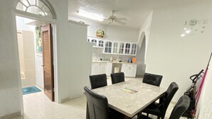 A dining area with a marble table and black chairs, a kitchen in the background, and a ceiling fan. - Island Castle Rentals - Saltwater Pool & Hot Tub- Lovely 3 Bedrooms  (Frederiksted)