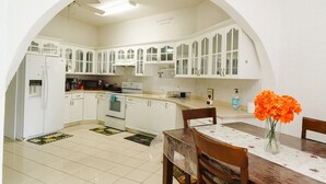 A kitchen with white cabinets, a microwave, and a dining table with chairs. - Island Castle Rentals - Saltwater Pool & Hot Tub- Lovely 3 Bedrooms  (Frederiksted)