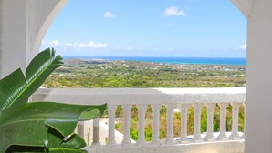 A balcony with a white balustrade overlooking a coastal landscape with greenery and the sea. - Island Castle Rentals - Saltwater Pool & Hot Tub- Lovely 3 Bedrooms  (Frederiksted)