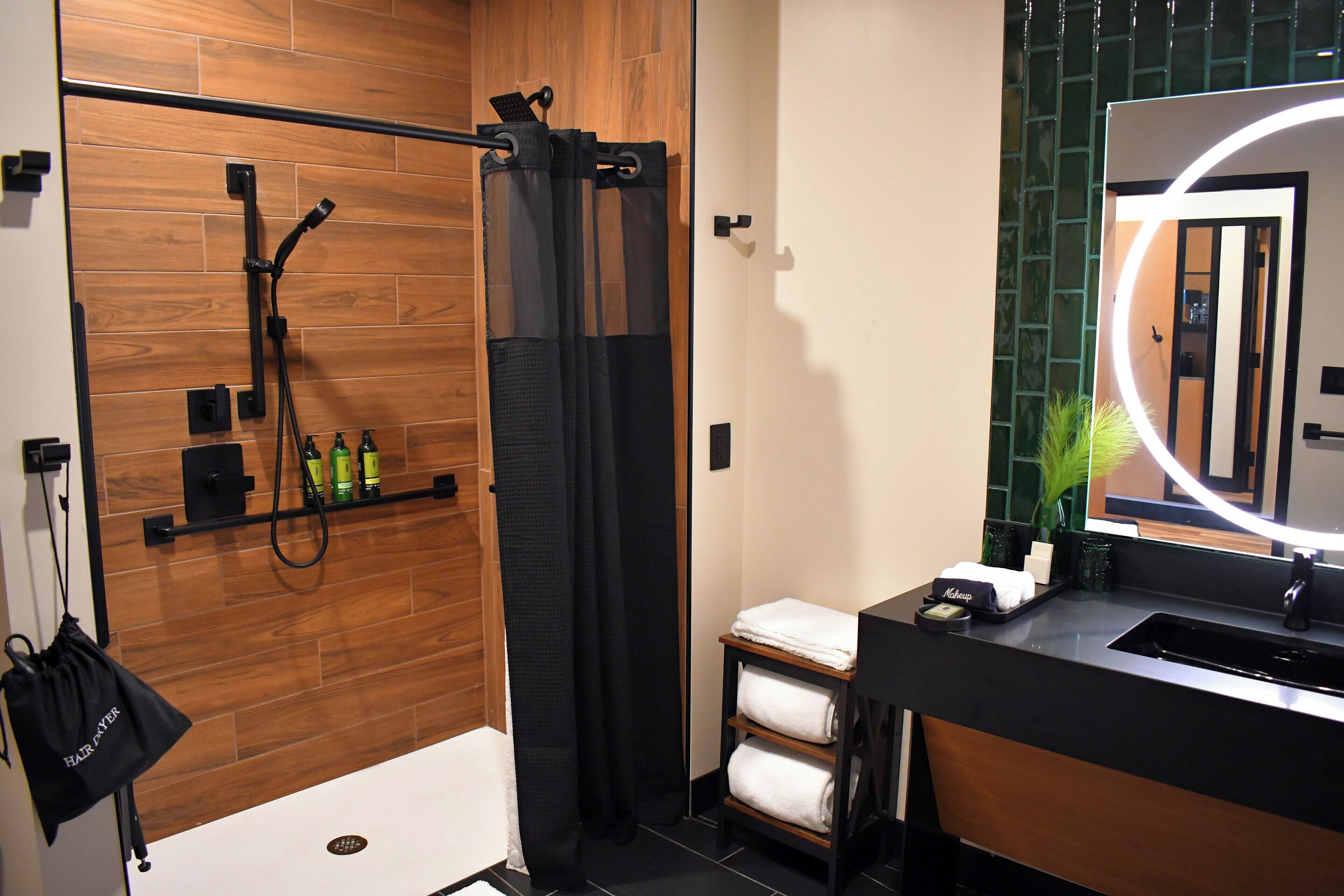 A modern bathroom with a wooden shower enclosure, a black towel rack, and a mirror with a circular light.
