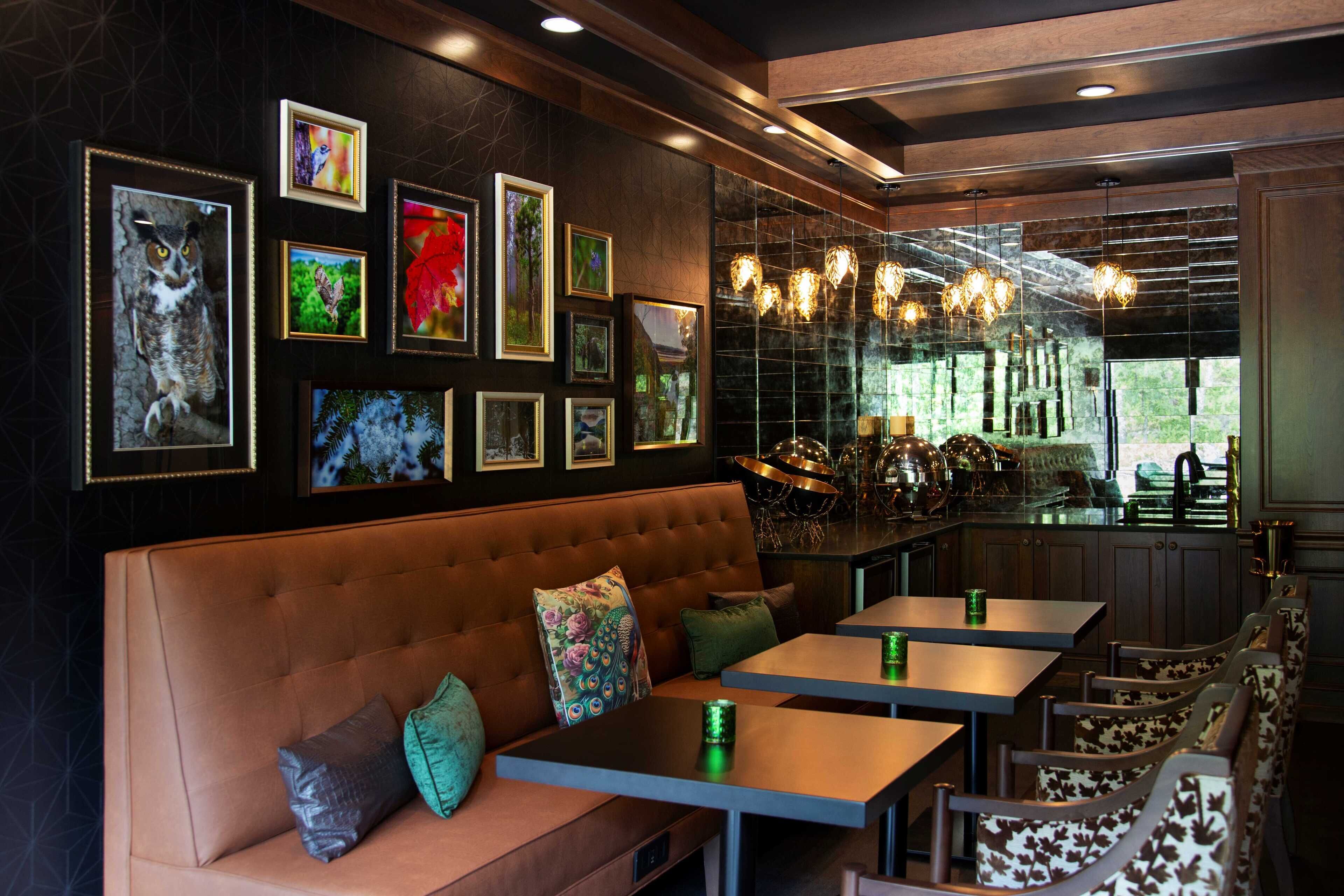 Interior de un restaurante con una cabina de cuero marrón, varias fotografías enmarcadas en la pared y una zona de bar con vistas a zonas verdes exteriores.