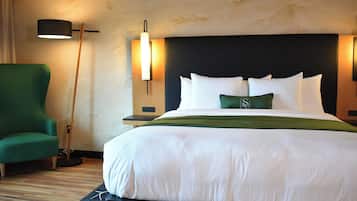 A hotel room with a large bed, a green armchair, a floor lamp, and two wall-mounted lamps.