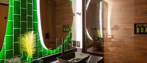 Un baño moderno con un espejo grande, pared de azulejos verdes, paneles de madera y un lavamanos negro.