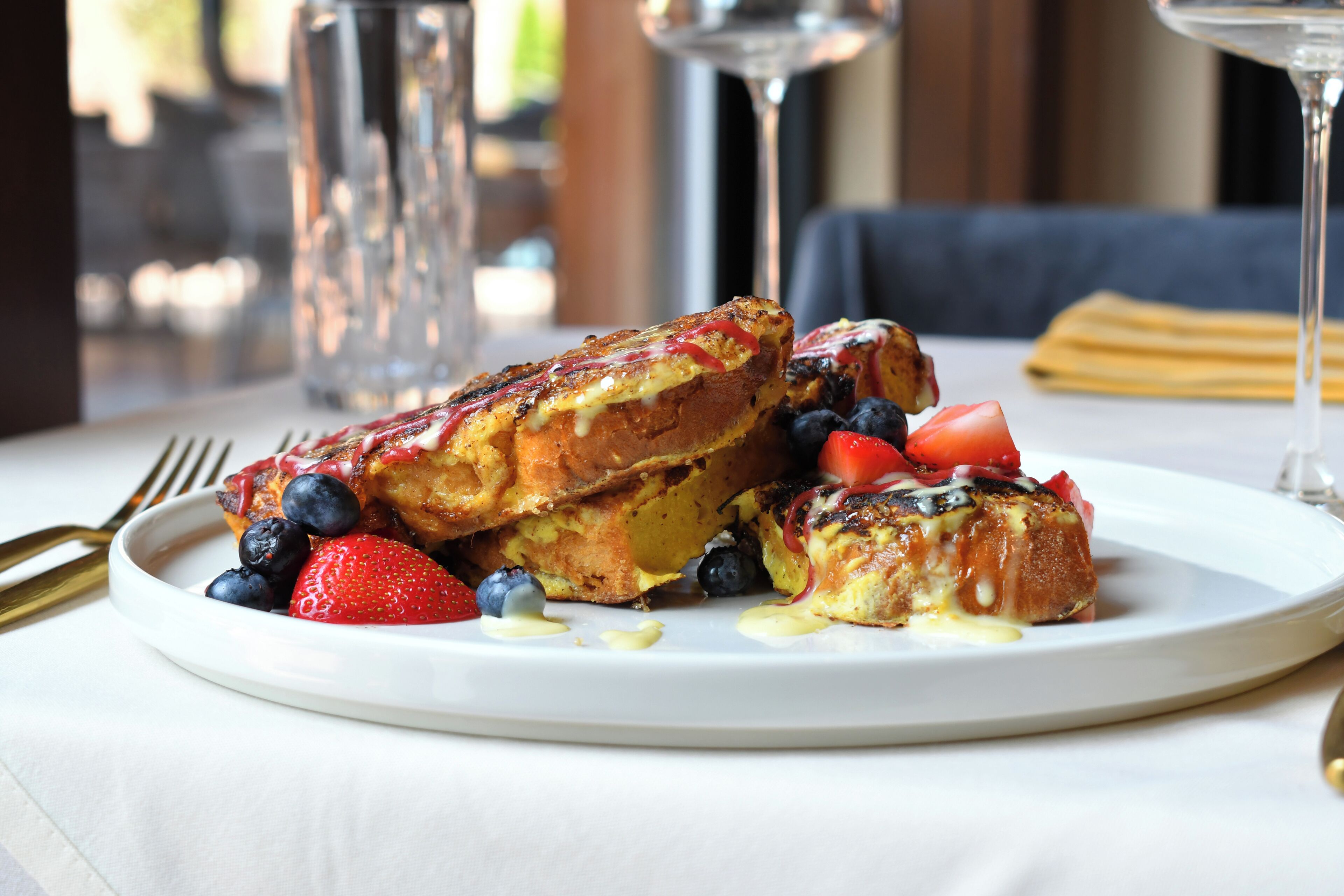 Une assiette de pain perdu garnie de myrtilles et de fraises, accompagnée d’un verre d’eau et d’un verre à vin.