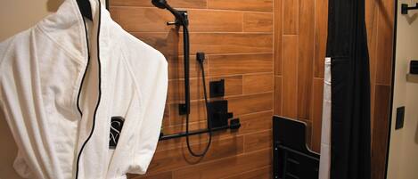 A bathroom with a wooden wall, a white robe hanging on a hook, and a shower area with a black curtain.