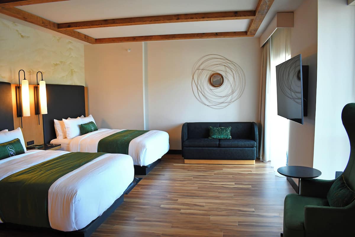 A hotel room with two beds, a sofa, a TV, and a wooden floor.