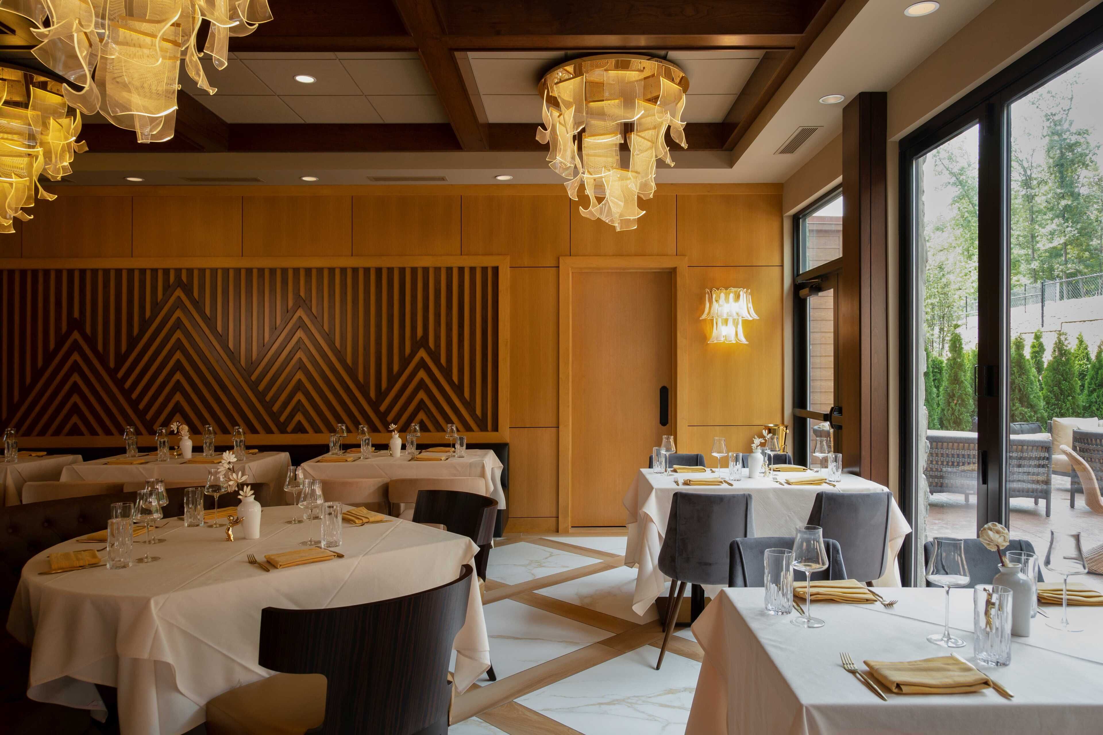 Un restaurante con mesas redondas dispuestas para comer, con manteles blancos y cubertería ordenada.