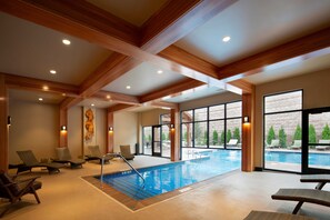 Relax by the pool surrounded by lounge chairs and a table, with views of the outdoors through large windows.