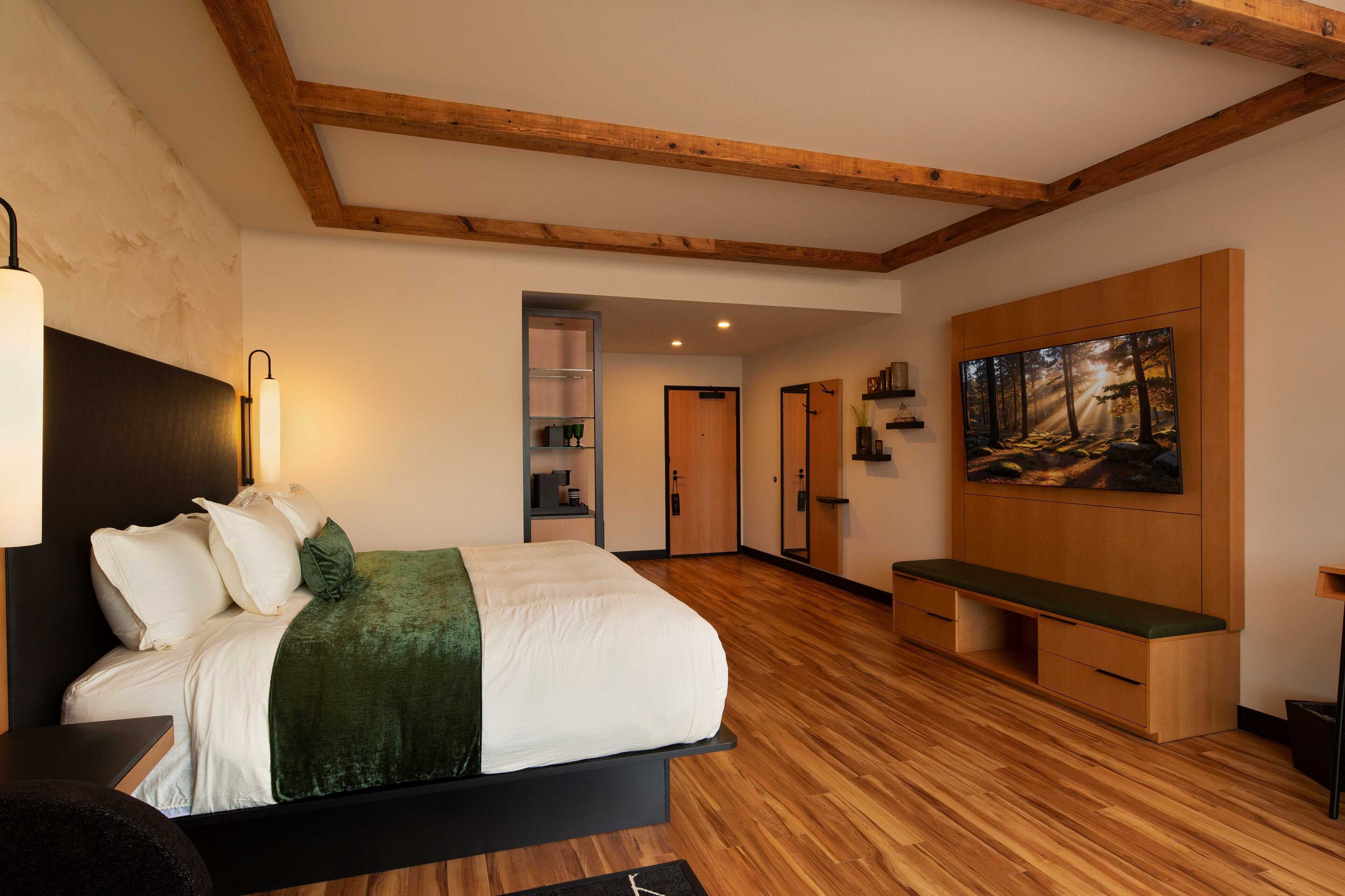 A modern bedroom with a wooden ceiling, a large bed with white bedding, a bench, and a painting on the wall.