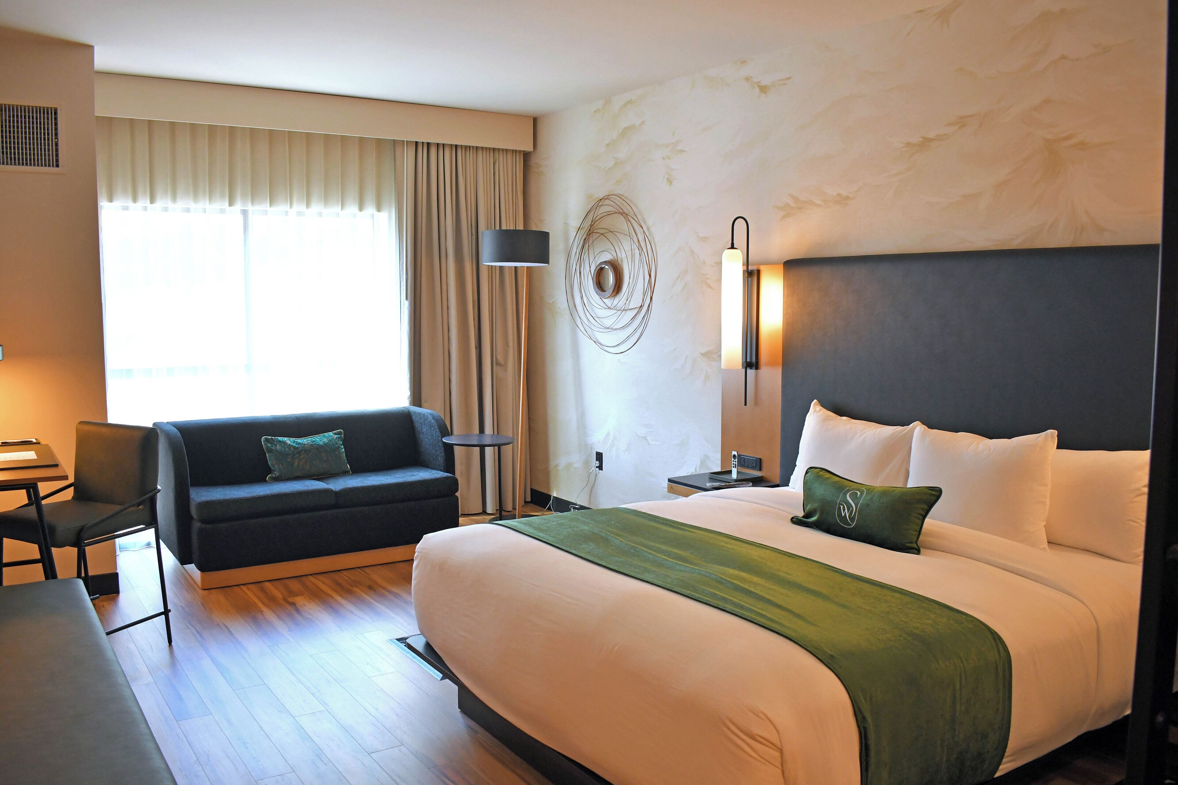 Una camera d'albergo con un letto grande, un divano, una scrivania e una lampada.