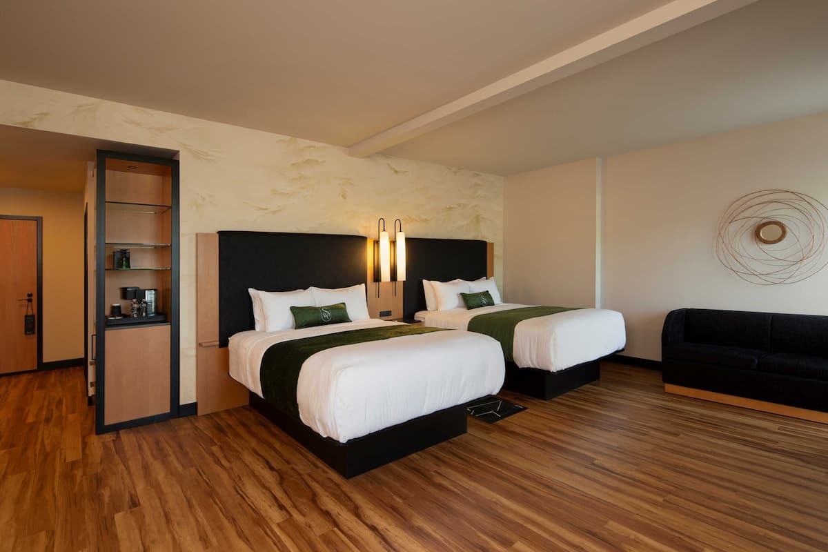 A hotel room with two beds, a black sofa, a wooden floor, and a wall with a circular design.
