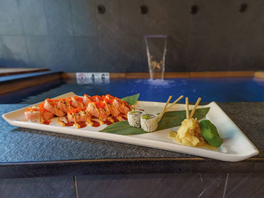 Uma seleção de sushi em um prato branco, com diversos rolinhos e nigiris sobre uma mesa escura.
