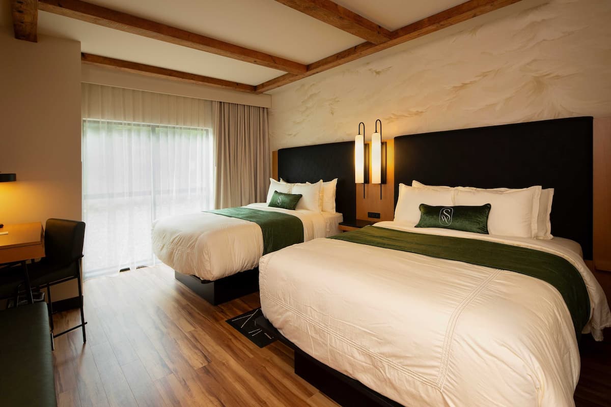 A hotel room with two beds, a desk, and a chair.