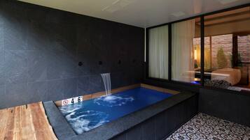 A modern bathroom with a blue-tiled bathtub, a wooden bench, and a large window with curtains.