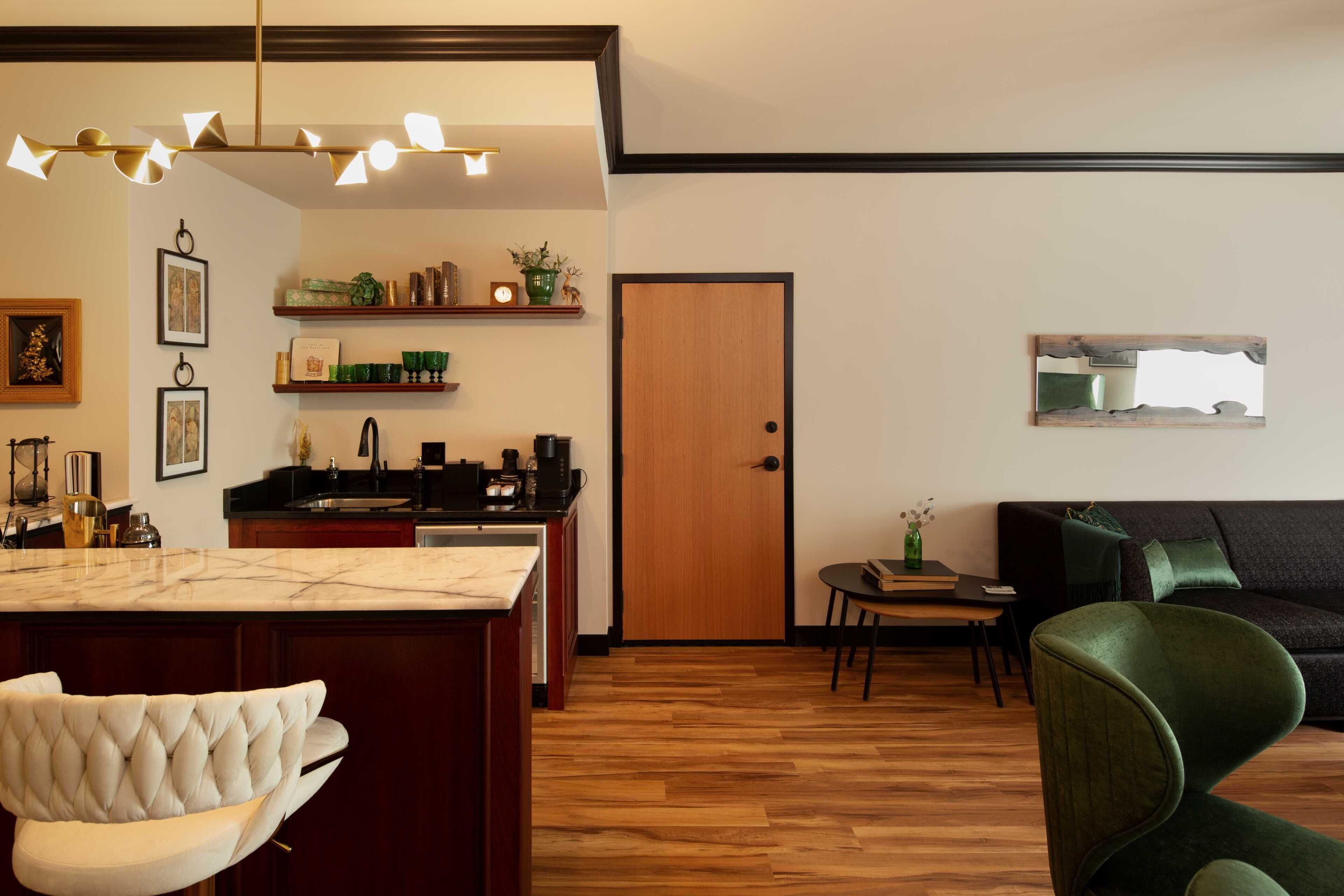 Une cuisine moderne dotée d’un plan de travail en marbre, d’un revêtement de sol en bois et d’un coin repas avec une chaise rembourrée de tissu vert et une petite table.