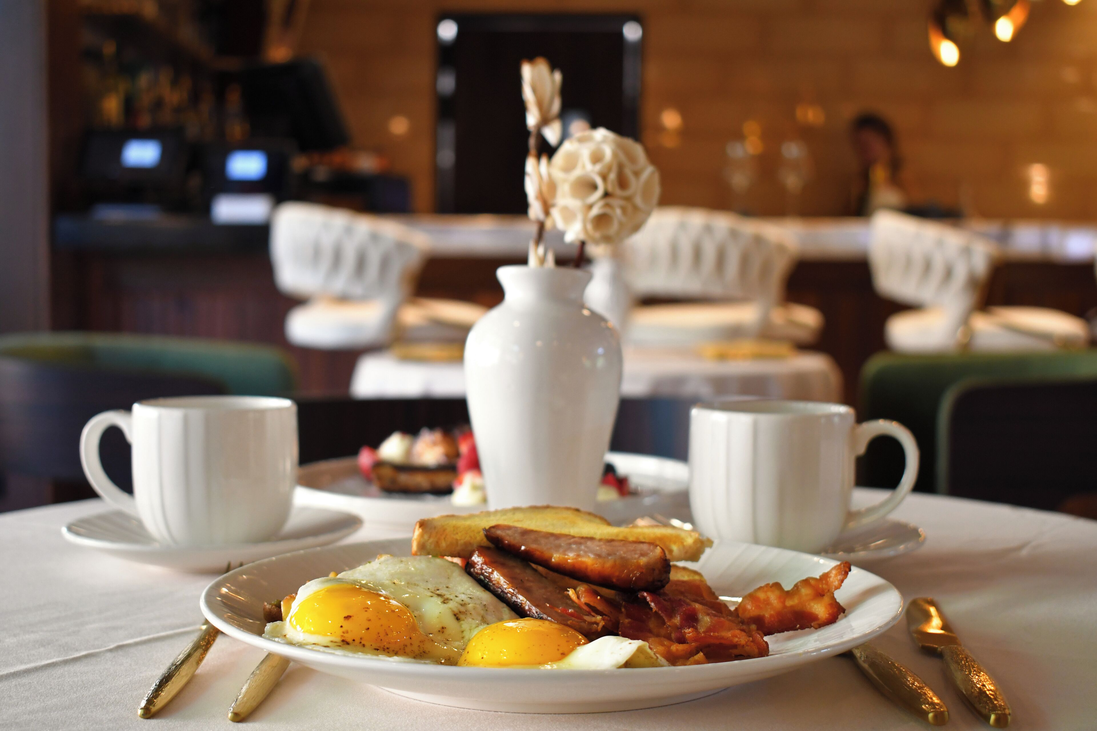 A breakfast plate with eggs, bacon, and toast on a table in a restaurant.