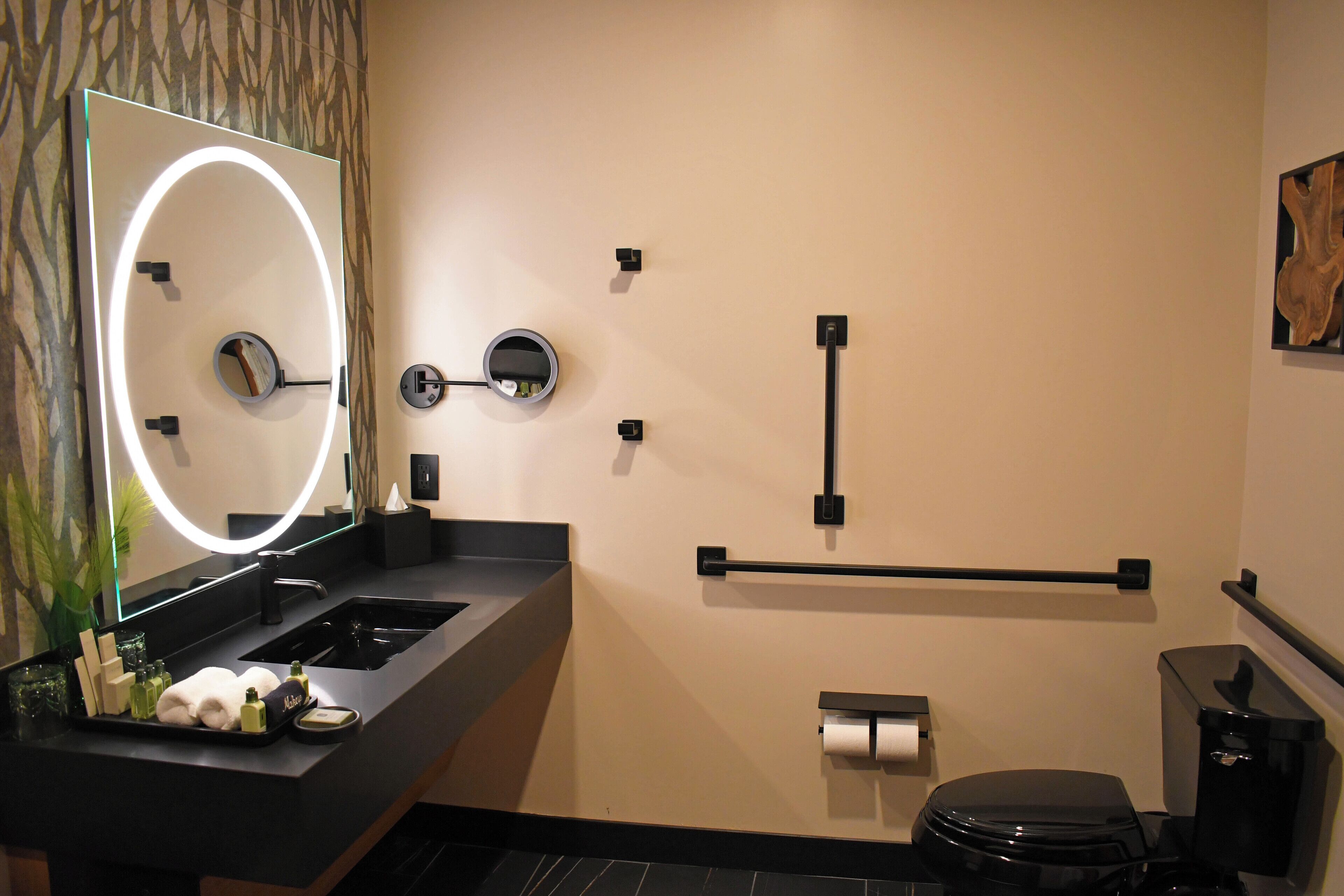 A modern bathroom with a black sink, a mirror with a light, a toilet, and a towel rack.