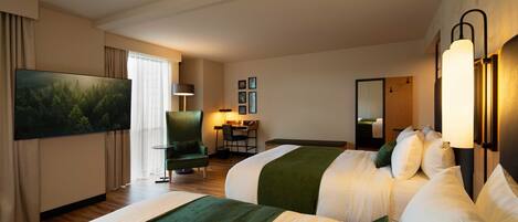A hotel room with two beds, a desk, a chair, a TV, and a large window.