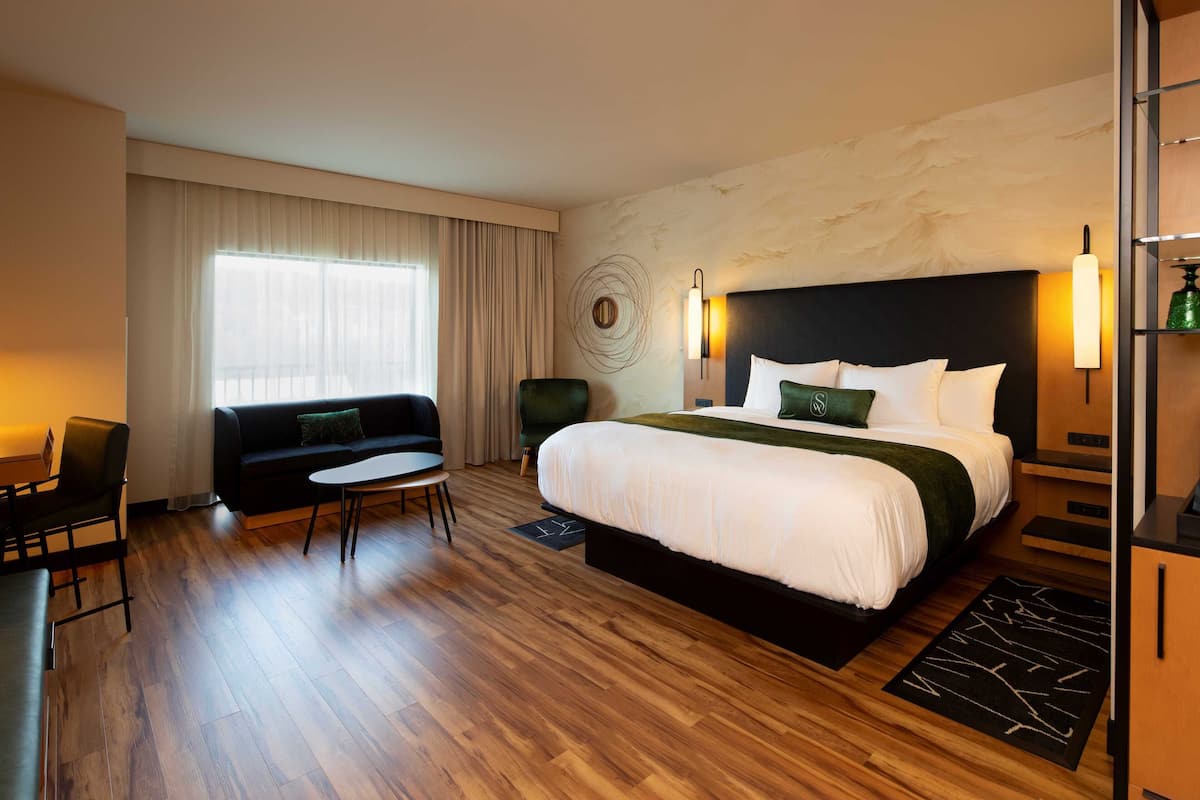 A hotel room with a large bed, a sofa, a small table, and a desk.