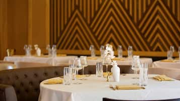 A dining area with round tables set for a meal, featuring white tablecloths, clear glassware, and gold napkins.