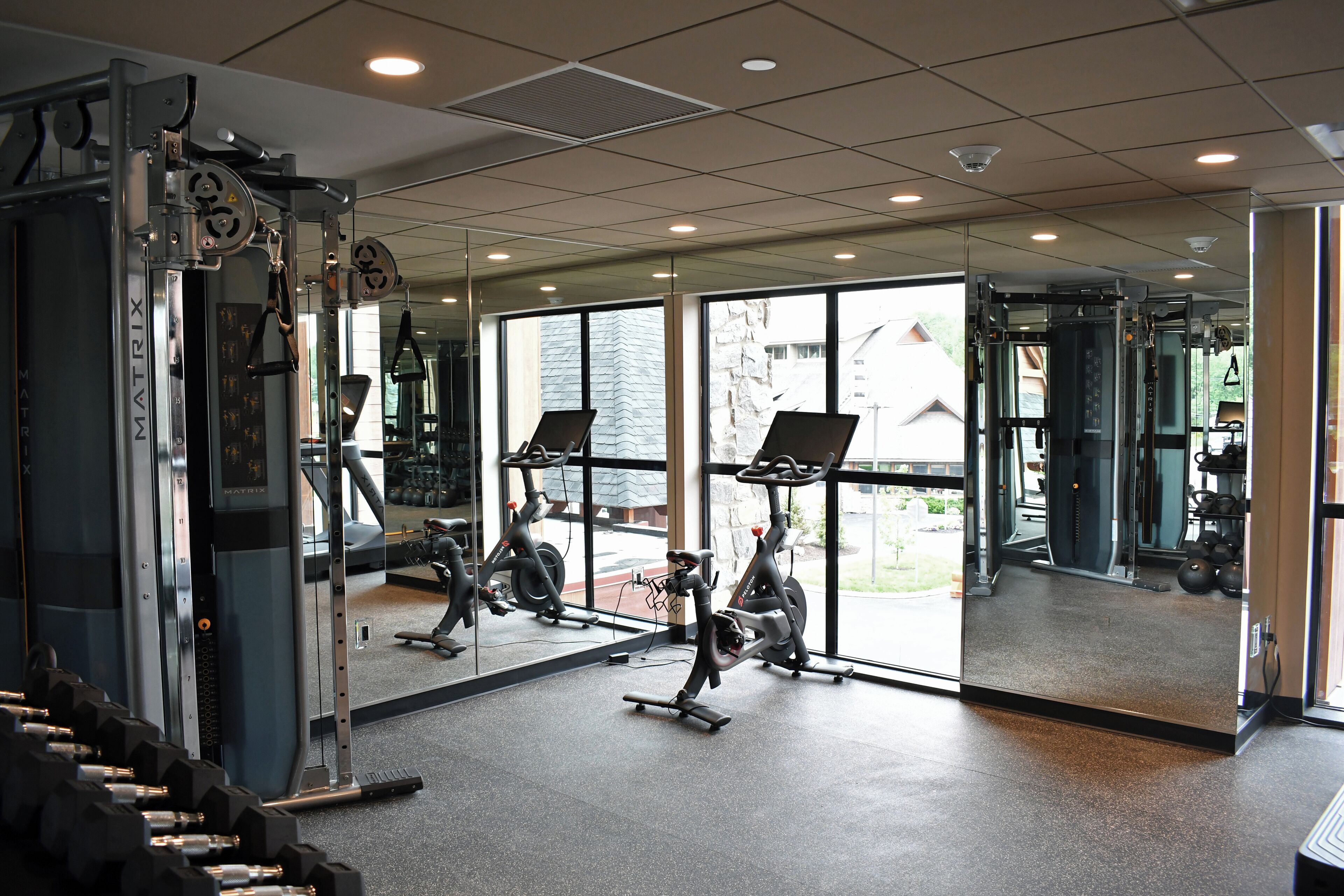 A gym with exercise equipment, large windows, and a mirrored wall.