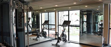 A gym with exercise equipment, large windows, and a mirrored wall.