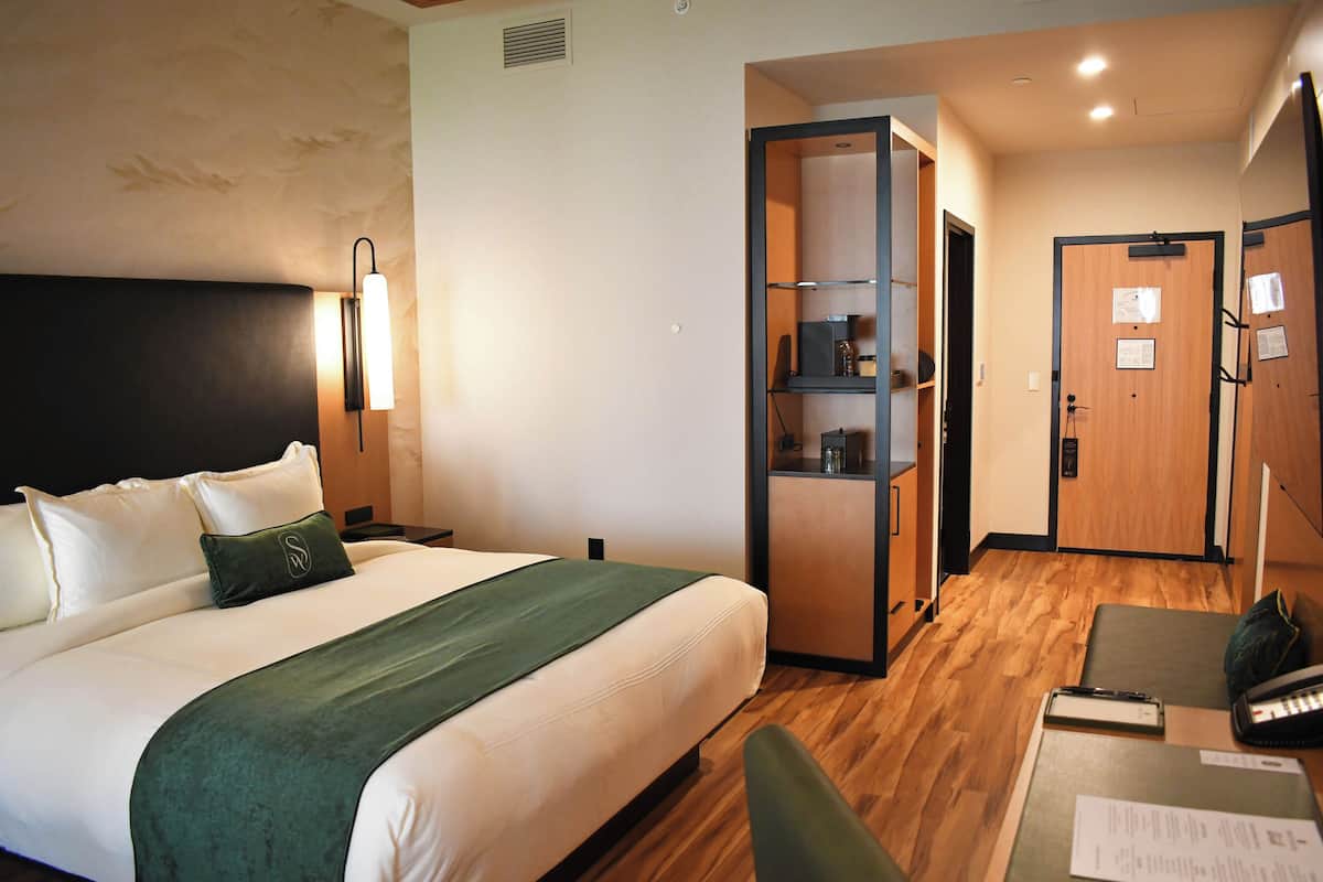 A hotel room with a bed, a desk, a chair, a wardrobe, and a mirror.
