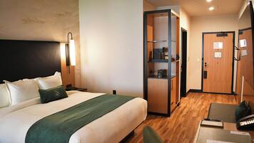 Una habitación de hotel con cama, escritorio, silla, armario y espejo.